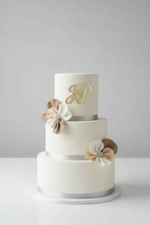 Wedding cake toppers custom acrylic initials topper on modern two tier wedding cake with neutral floral decorations on plain light background