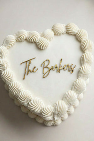 Wedding cake toppers personalized acrylic last name sign on heart shaped wedding cake with piped white frosting on soft light background